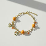 Gold bracelet with orange beads and floral charms on a light background