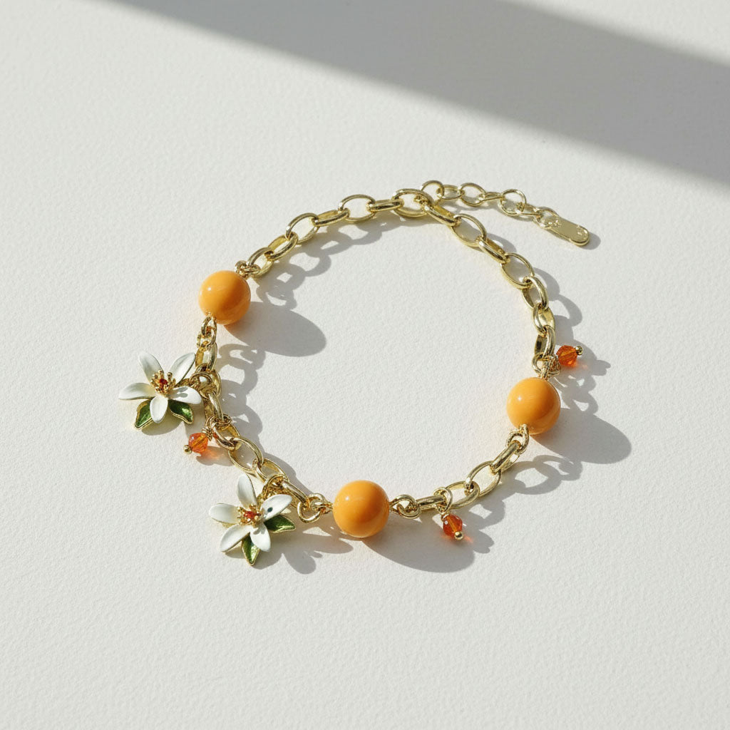 Gold bracelet with orange beads and floral charms on a light background