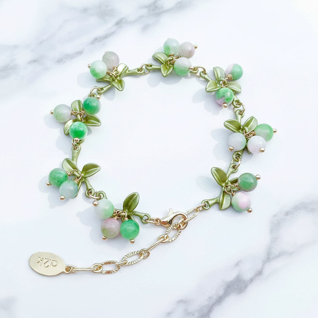 Green beaded bracelet with gold chain on a marble surface