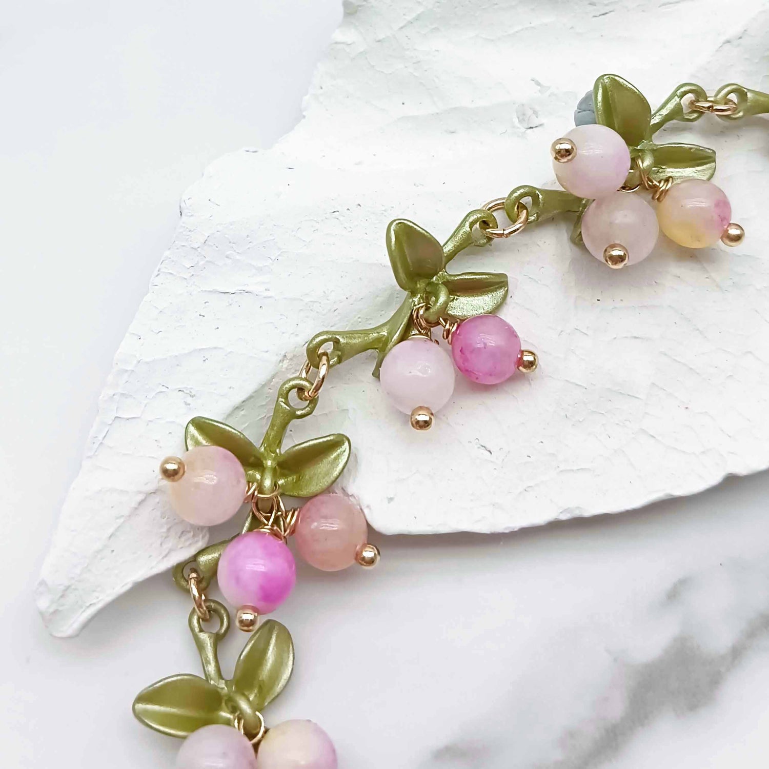 Bracelet with pink beads and gold accents on a white leaf background