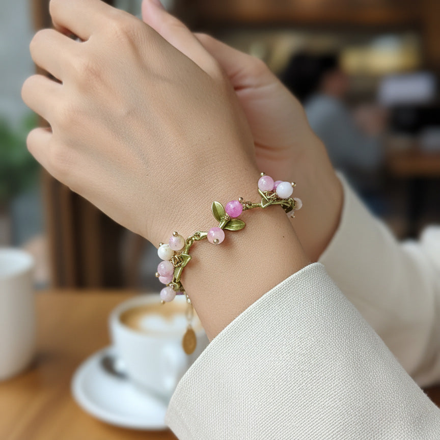 Hand wearing a decorative bracelet with pink beads and green leaves, blurred cafe background