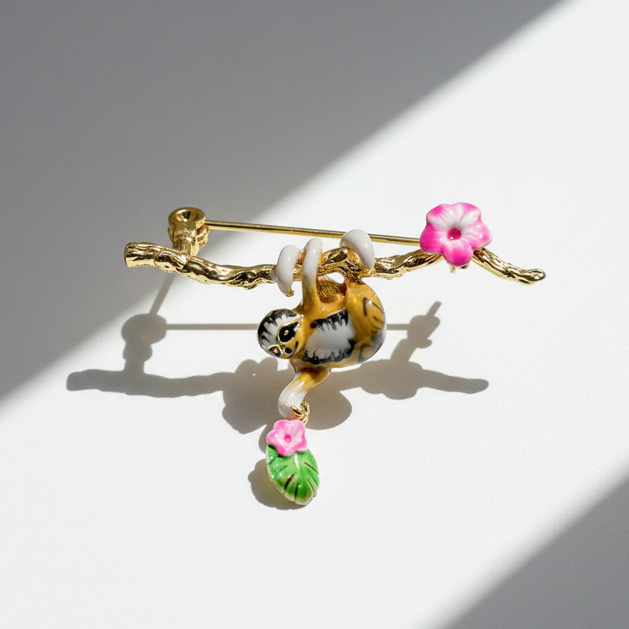Jewelry brooch with a gold branch, sloth, and pink flowers on a white background