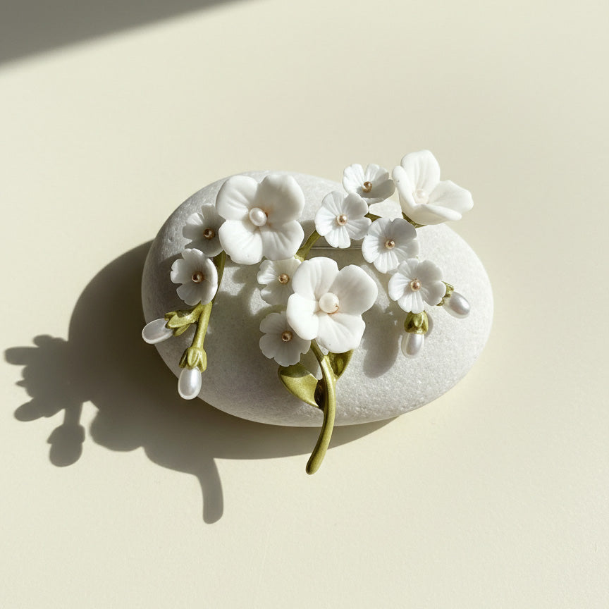 White porcelain flower brooch with hand-painted enamel leaves and pearl details, styled on stone surface