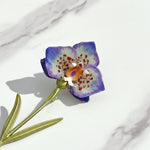 Close-up of hand-painted purple resin flower brooch with green leaves