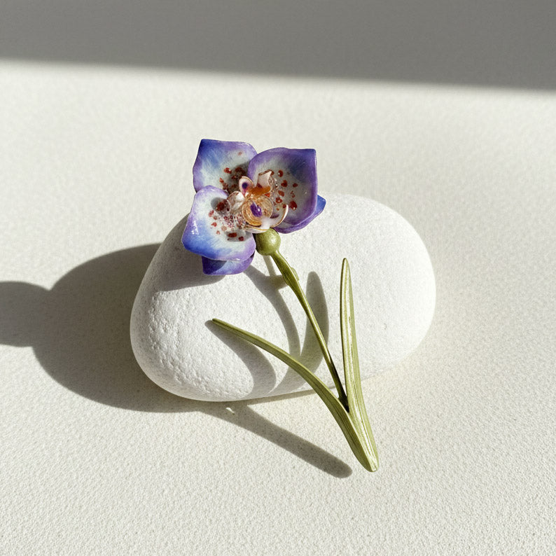 Artisan purple floral brooch with green stem on a white stone surface