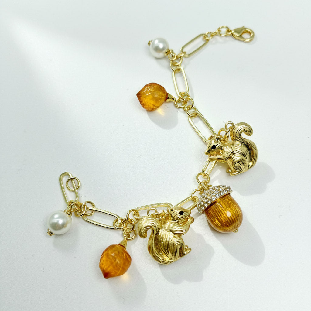 Gold bracelet with charms including a squirrel, acorns, and pearls on a white background