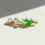 Jewelry piece with pearls and green leaf design on a light background
