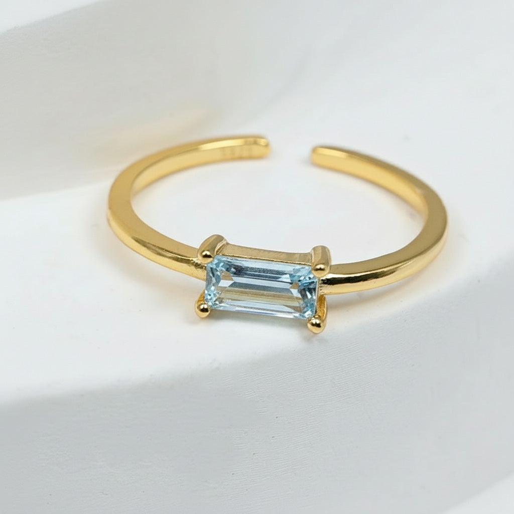 Gold-plated silver adjustable ring with rectangular light blue CZ birthstone, minimalist modern design by A2K London.