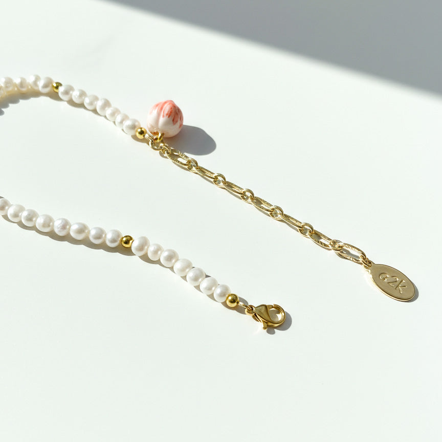 Adjustable freshwater pearl bracelet with gold extender chain and peach charm on a light surface