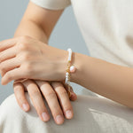 Person wearing a pearl bracelet with peach charm on a neutral background