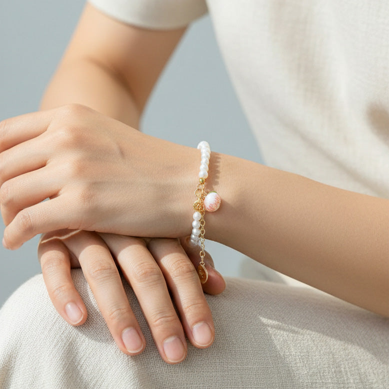 Person wearing a pearl bracelet with peach charm on a neutral background
