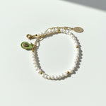 Adjustable freshwater pearl bracelet with gold extender chain and avocado charm on a white background