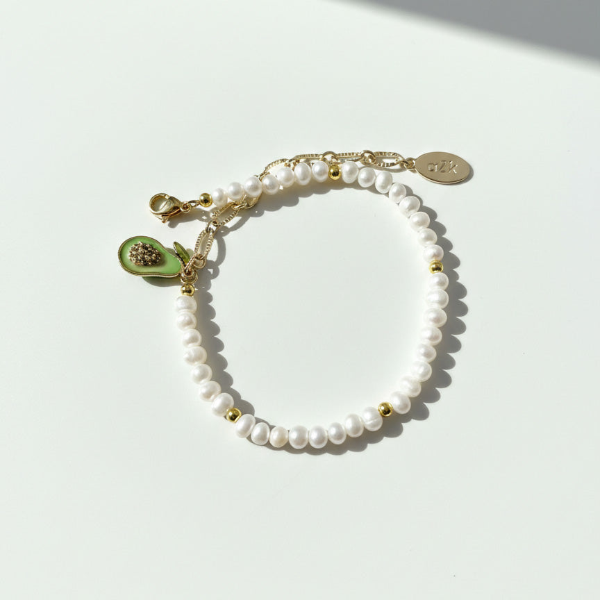 Adjustable freshwater pearl bracelet with gold extender chain and avocado charm on a white background