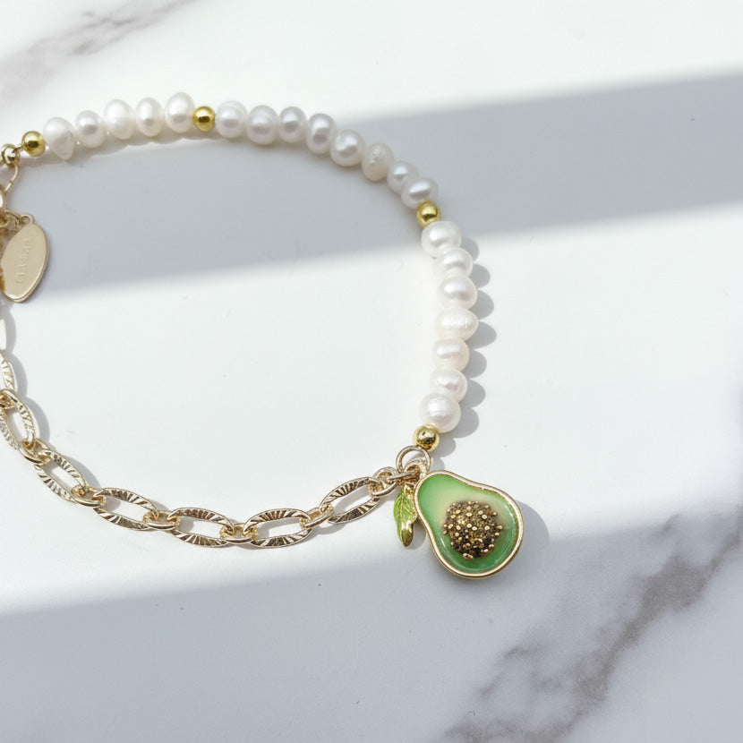 Close-up of enamel avocado charm with cubic zirconia on freshwater pearl bracelet on a marble surface