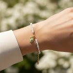 Close-up of a wrist wearing an enamel avocado charm with cubic zirconia on freshwater pearl bracelet against a blurred natural background