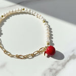 Close-up of red enamel apple charm on freshwater pearl bracelet on a marble surface