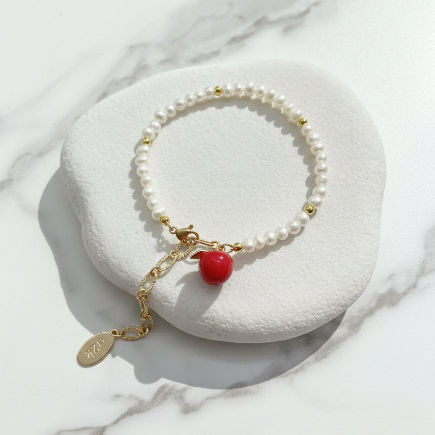 Adjustable freshwater pearl bracelet with gold extender chain and apple charm on a white stone surface