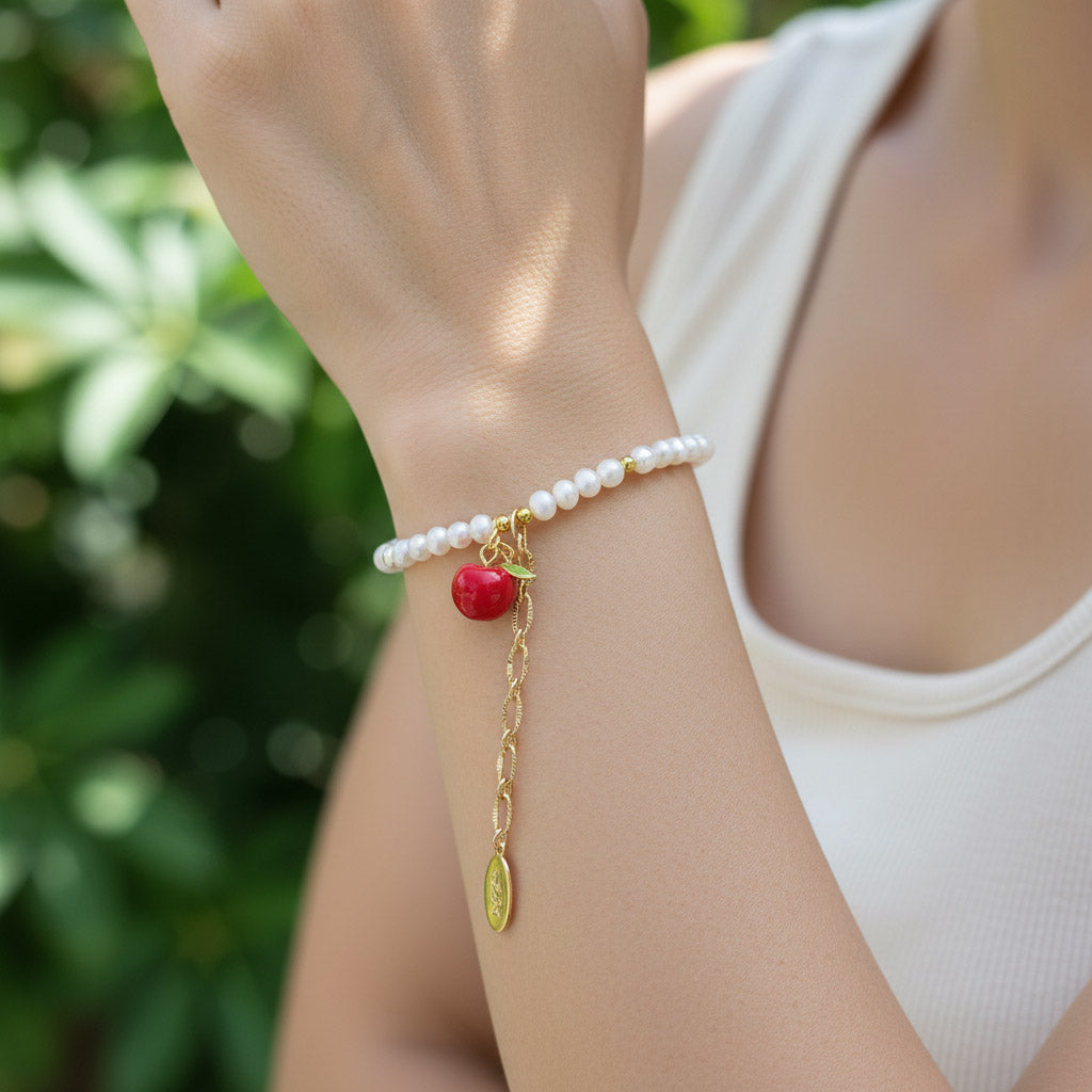 Model wearing freshwater pearl bracelet with red apple charm and gold chain