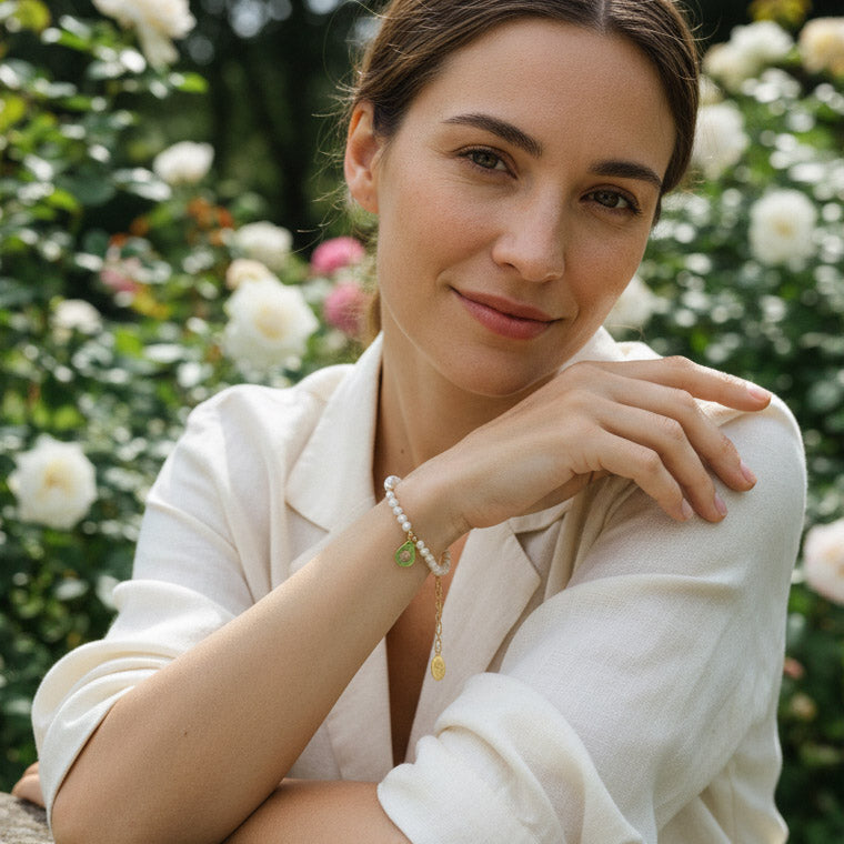 Woman in a white outfit with a CZ paved avocado charm bracelet standing in a garden with flowers.