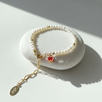 Freshwater pearl bracelet with pavé red pomegranate charm in 18K gold-plated brass on a white stone surface