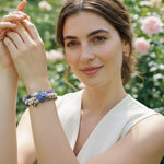 Woman wearing a layered amethyst pearl and cloisonné beaded bracelet set with a garden background