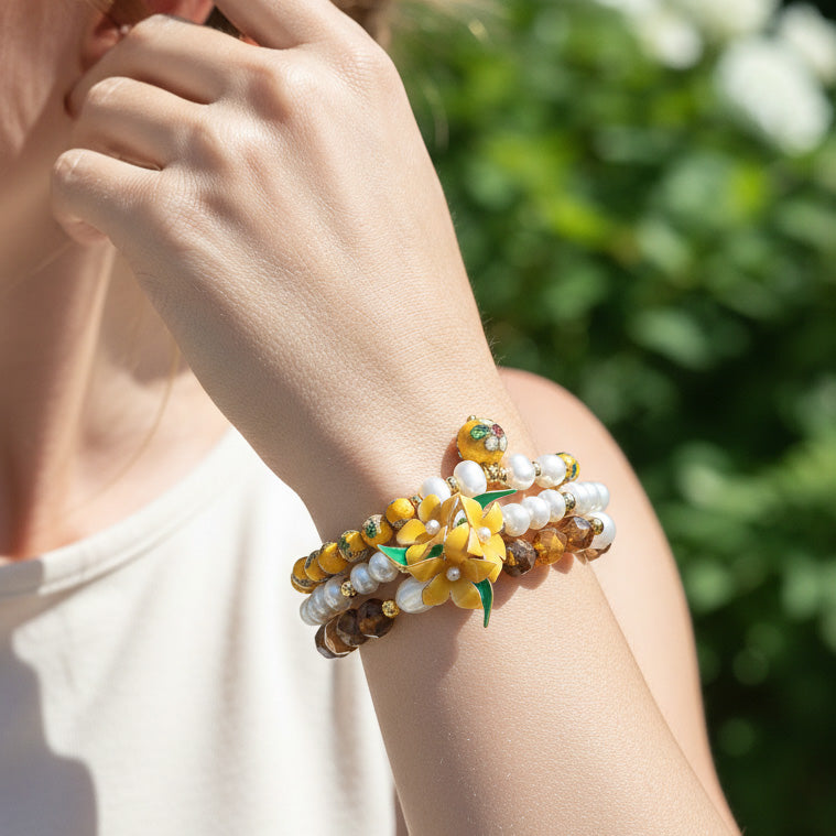 Close-up of a hand wearing a yellow resin flower with pearls and tiger eye beads with a blurred green background