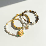 Layered yellow opal and tiger eye bracelet set with cloisonné beads on a light background