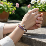 Close-up of a person's wrist wearing an amethyst and freshwater pearl bracelet set with handcrafted resin flower with plants in the background.