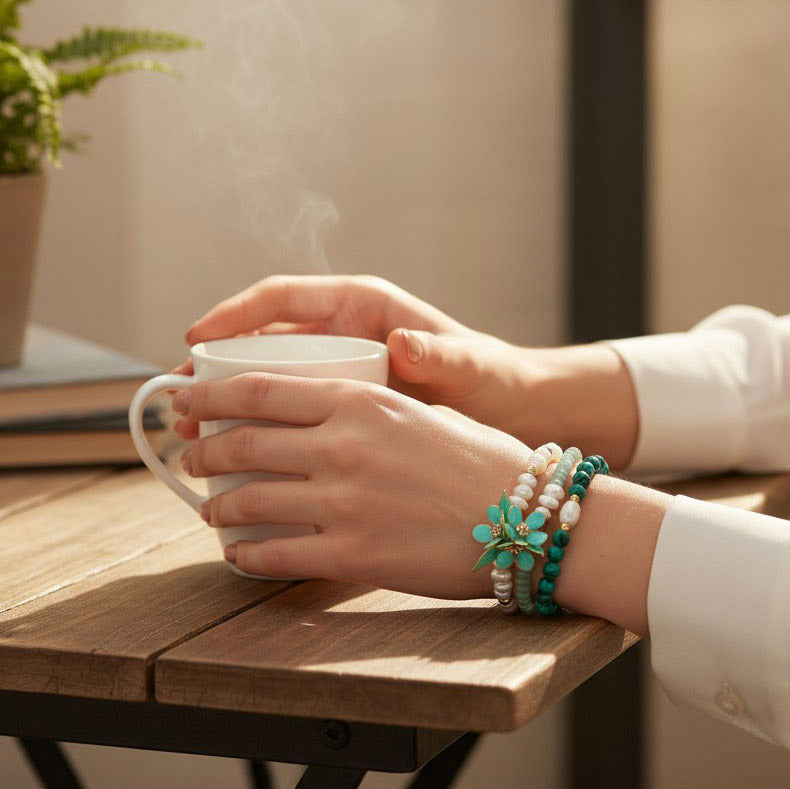 Person holding a steaming cup of coffee with bracelets on a wooden table.