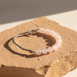 8mm Rose Quartz bracelet with stainless steel hook on natural stone background in warm sunlight