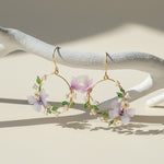 Gold hoop earrings with floral designs on a white wooden surface