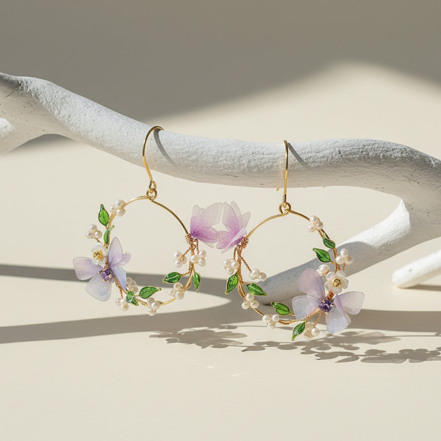Gold hoop earrings with floral designs on a white wooden surface