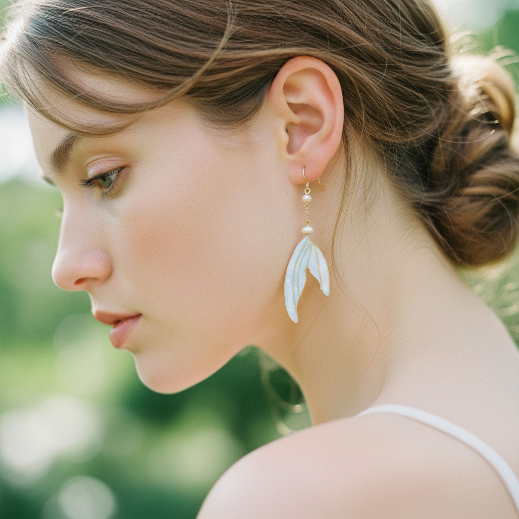 Woman wearing a pair of white wing-shaped earrings with a blurred green background