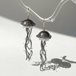 Jellyfish-shaped earrings on a clear stand with a gray background