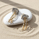 Jellyfish-shaped earrings with gold and silver details on a white stone in sand