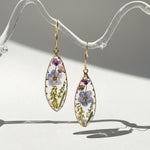 Teardrop-shaped earrings with floral design on a clear stand.