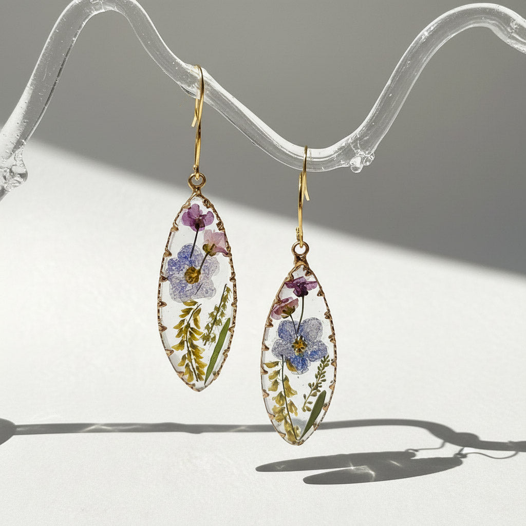 Teardrop-shaped earrings with floral design on a clear stand.