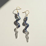 Spiral-shaped earrings with blue gemstones on a light background