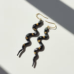 Serpentine earrings with gold accents on a light background