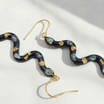 Snake-shaped earrings with gold accents on a light background