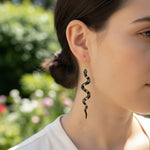 Woman wearing a black and gold spiral earring with a blurred garden background