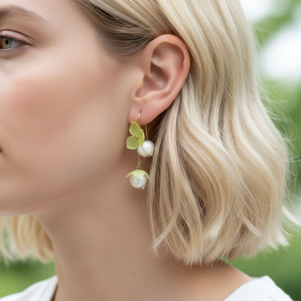 Close-up of a woman wearing a pair of earrings with green leaves and white flowers.