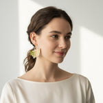 Woman wearing a gold earring with a green leaf on a plain background