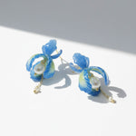 Blue orchid petal earrings with pearls and gold chain drops, handcrafted floral jewelry on white background.
