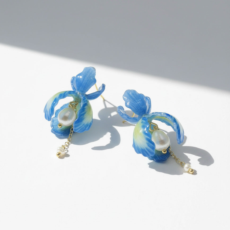 Blue orchid petal earrings with pearls and gold chain drops, handcrafted floral jewelry on white background.