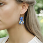 Model wearing blue orchid flower earrings with pearls and gold chain drops, elegant handcrafted floral jewelry.