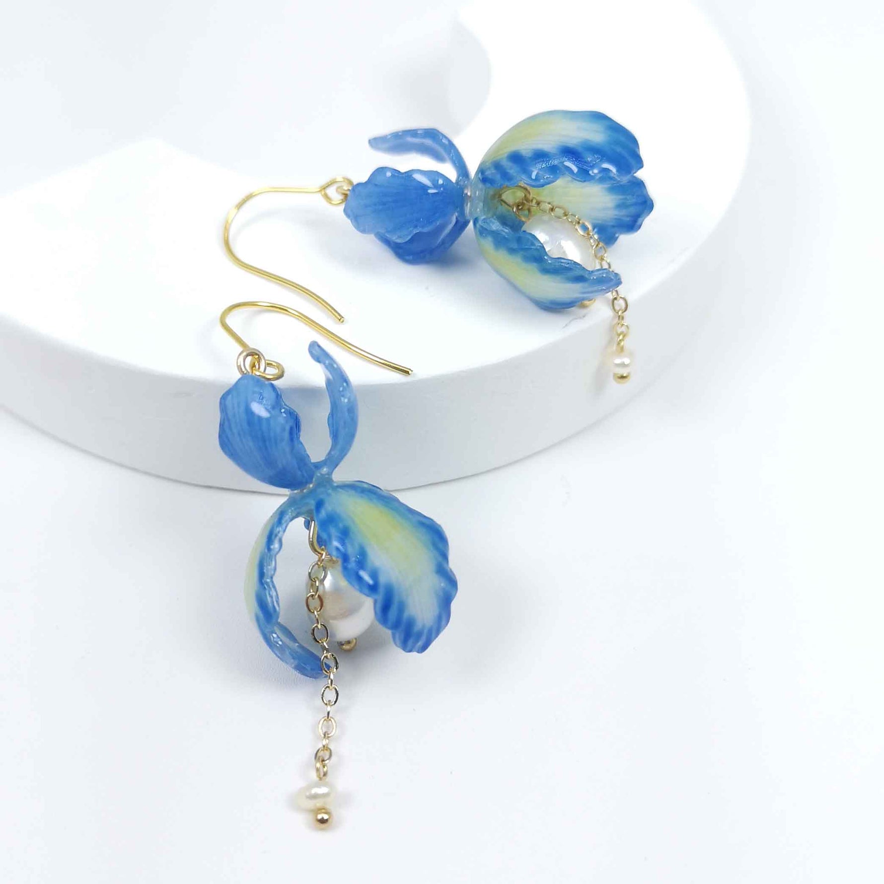 Blue iris flower drop earrings with handpainted resin petals, gold-plated hooks, faux pearl center, and dangling freshwater pearl chain on white background