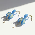 Blue orchid petal drop earrings with pearl and gold chain details, handcrafted floral jewelry on white background.