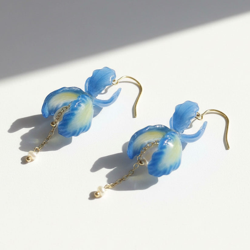 Blue orchid petal drop earrings with pearl and gold chain details, handcrafted floral jewelry on white background.
