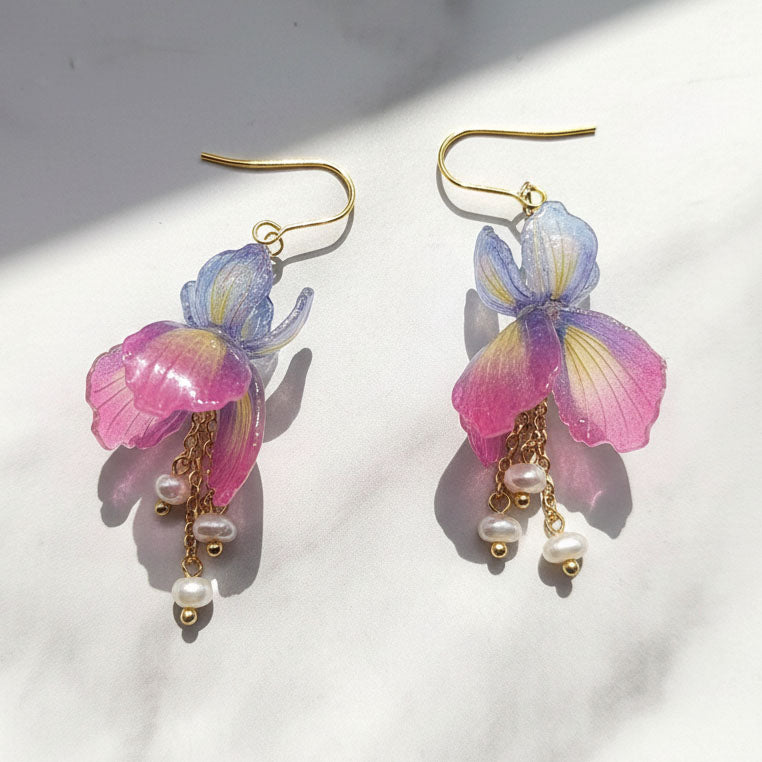Pair of floral earrings with pink and purple flowers and pearl-like beads on a white background